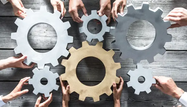 6 Zahnräder, die von verschiedenen Händen gehalten werden